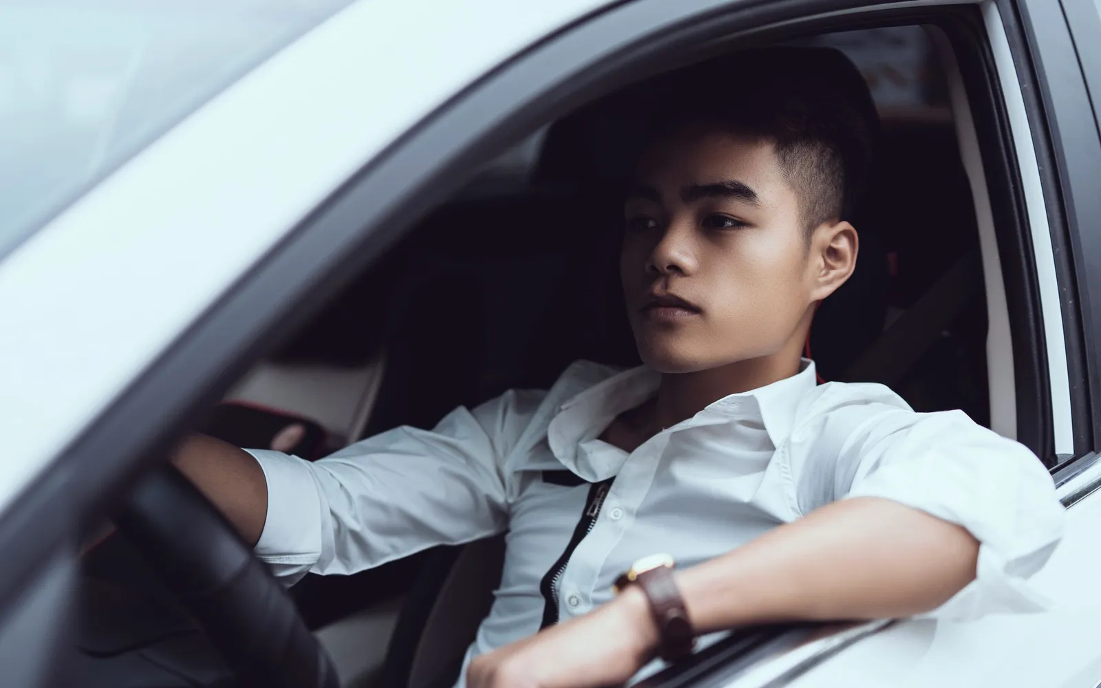 Chàng trai châu Á ngồi sau vô-lăng chiếc xe màu trắng