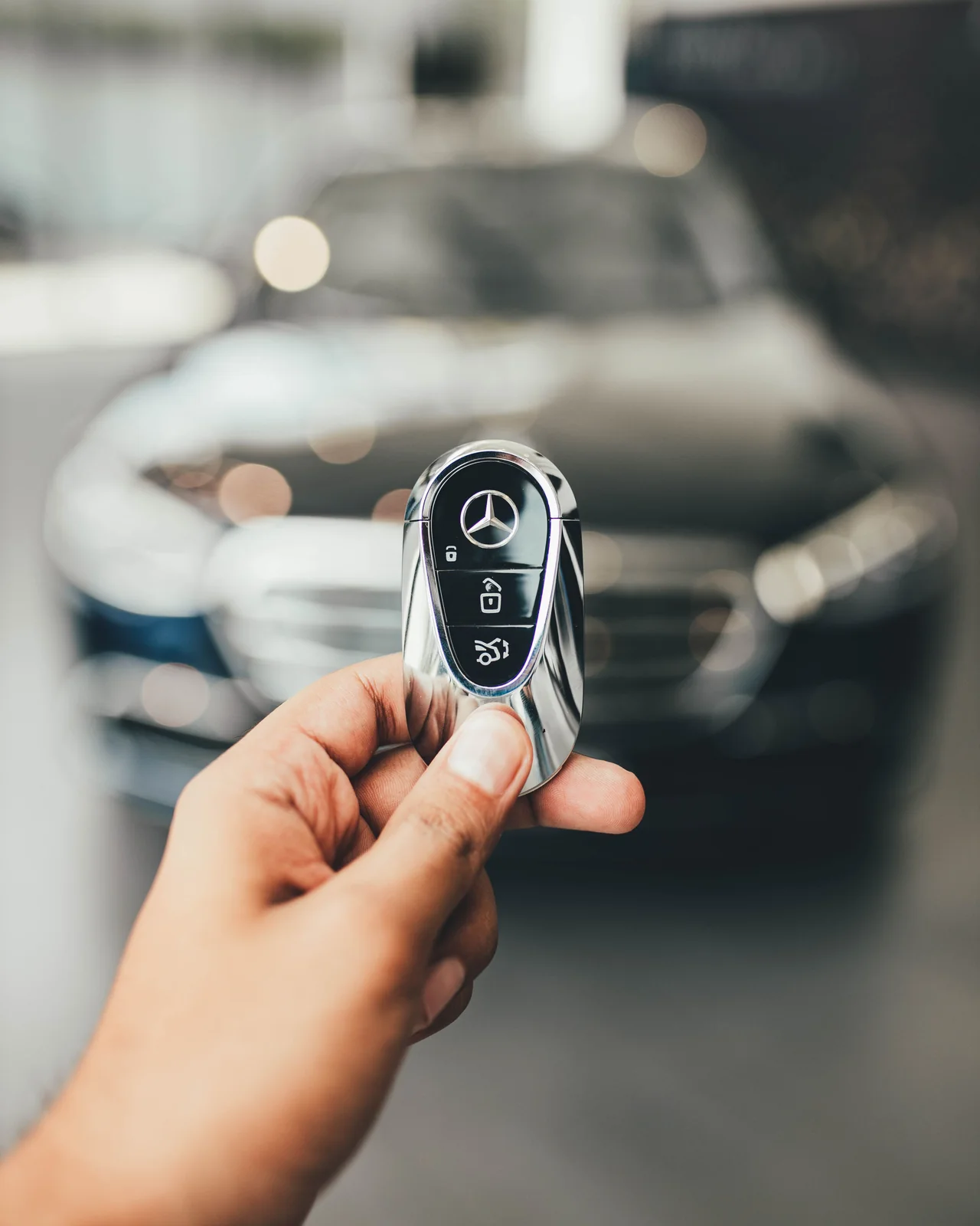 Bàn tay cầm chìa khoá Mercedes mới trước xe trong showroom
